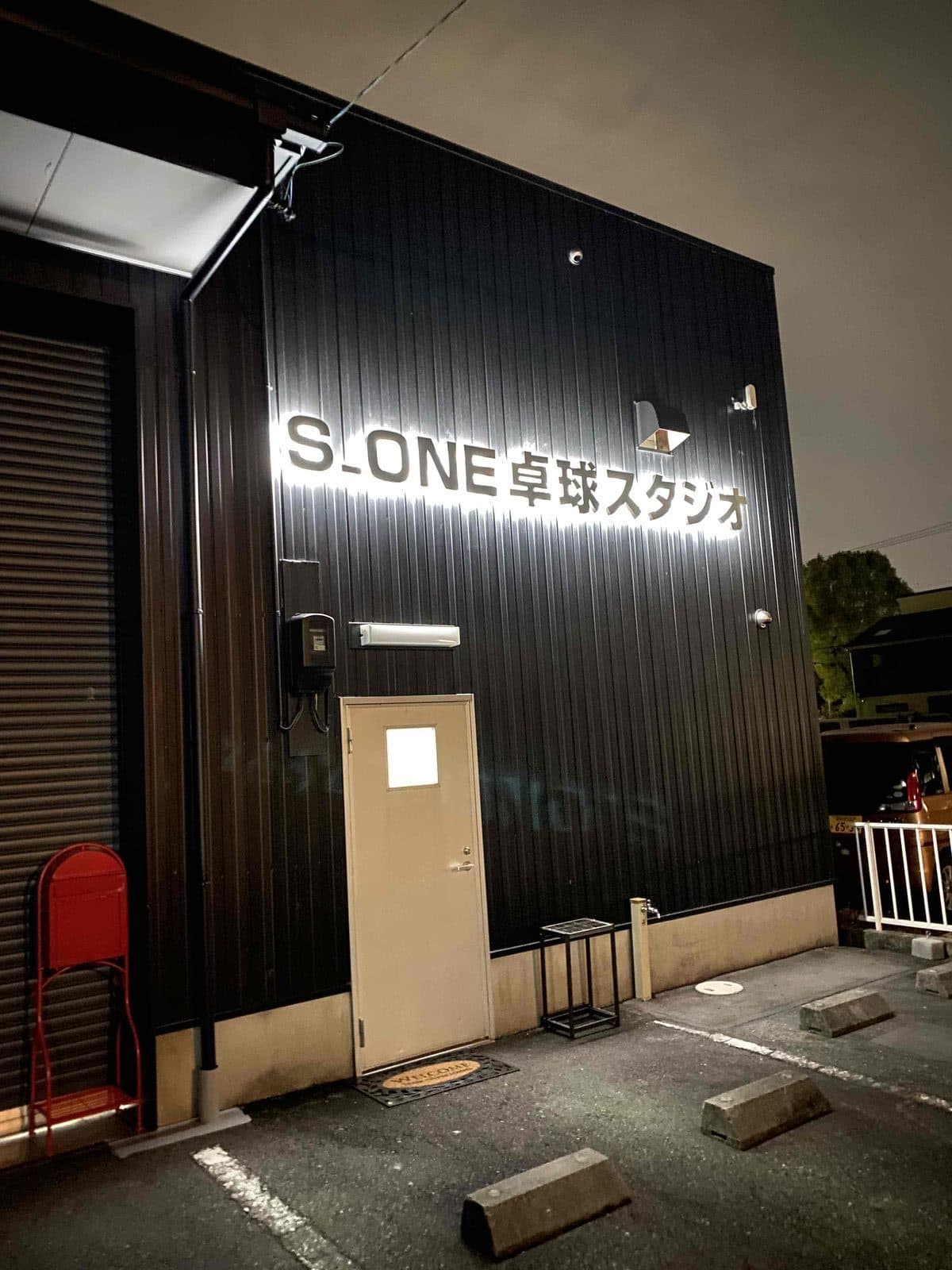 夜に看板が光るS_ONE卓球スタジオの入口。クリーム色の扉から入る